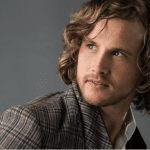 Stylish man with wavy hair in a modern haircut, wearing a plaid jacket, showcasing one of the top men's haircut trends for 2024